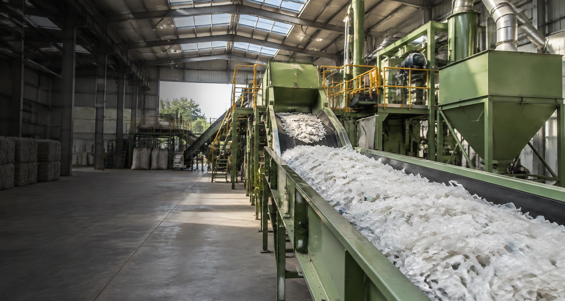 Illustrative plastic recycling facility with processing machinery and a conveyor of recovered plastic